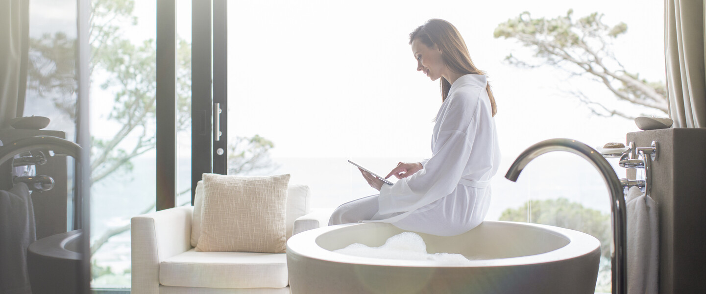 Frau mit Tablet sitzt auf Badewanne