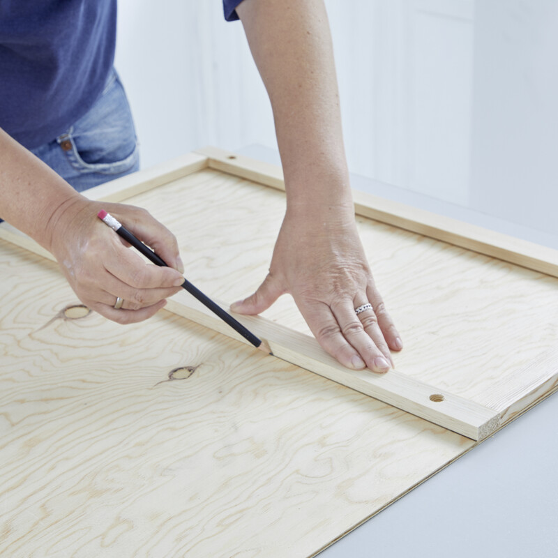 Eine Personen macht mit einem Bleistift Markierungen auf Holz