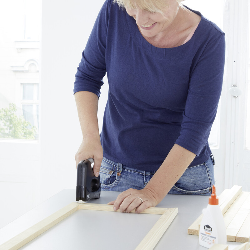 Eine blonde Frau fixiert Rechteckleisten mit einem Tacker aneinander.