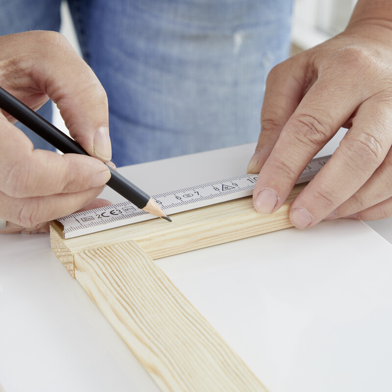 Mit einem Zollstock wird ein Stück Holz gemessen und mit einem Bleistift markiert.