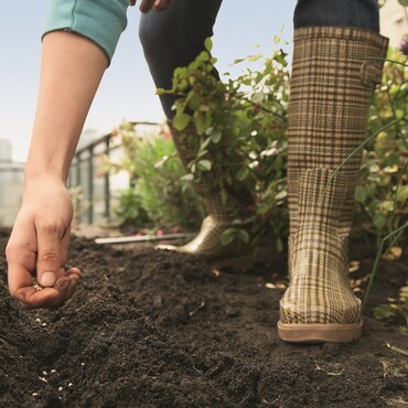Person in Gummistiefel verteilt Samen in Beet