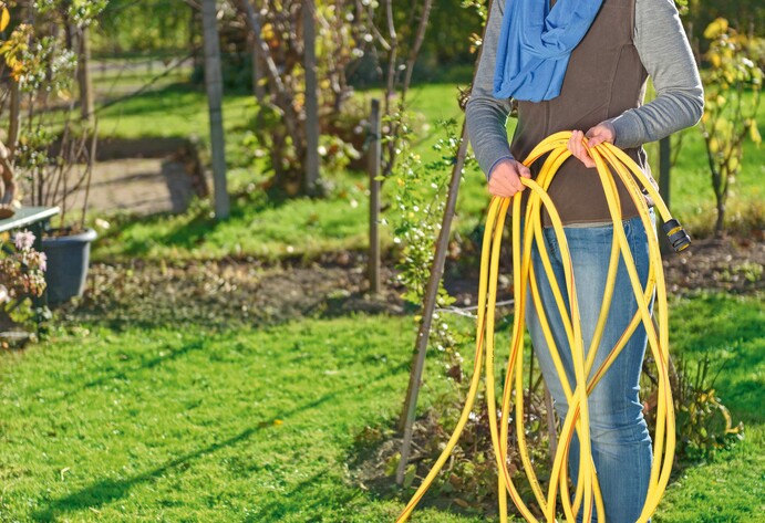 Frau rollt Gartenschlauch auf