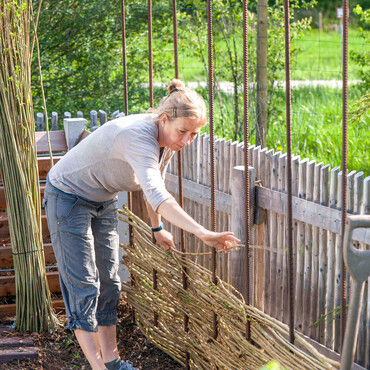 Eine Frau baut eine Rankhilfe aus Weide
