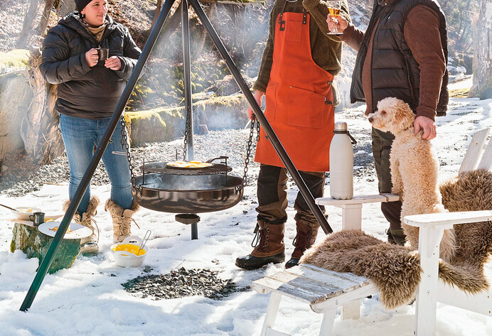 Drei Personen mit Hund grillen im Winter