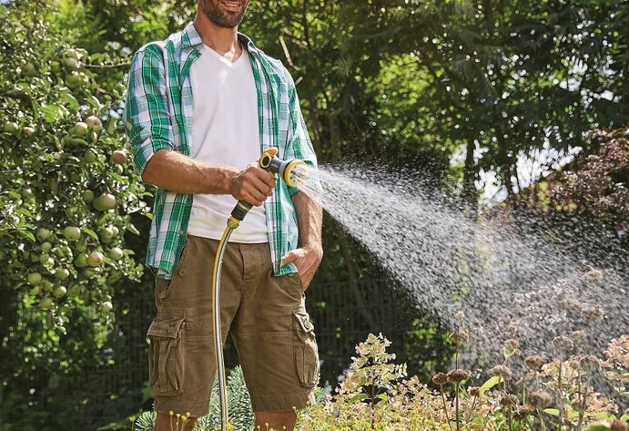 Mann bewässert Plfanzen im Garten mit einem Gartenschlauch