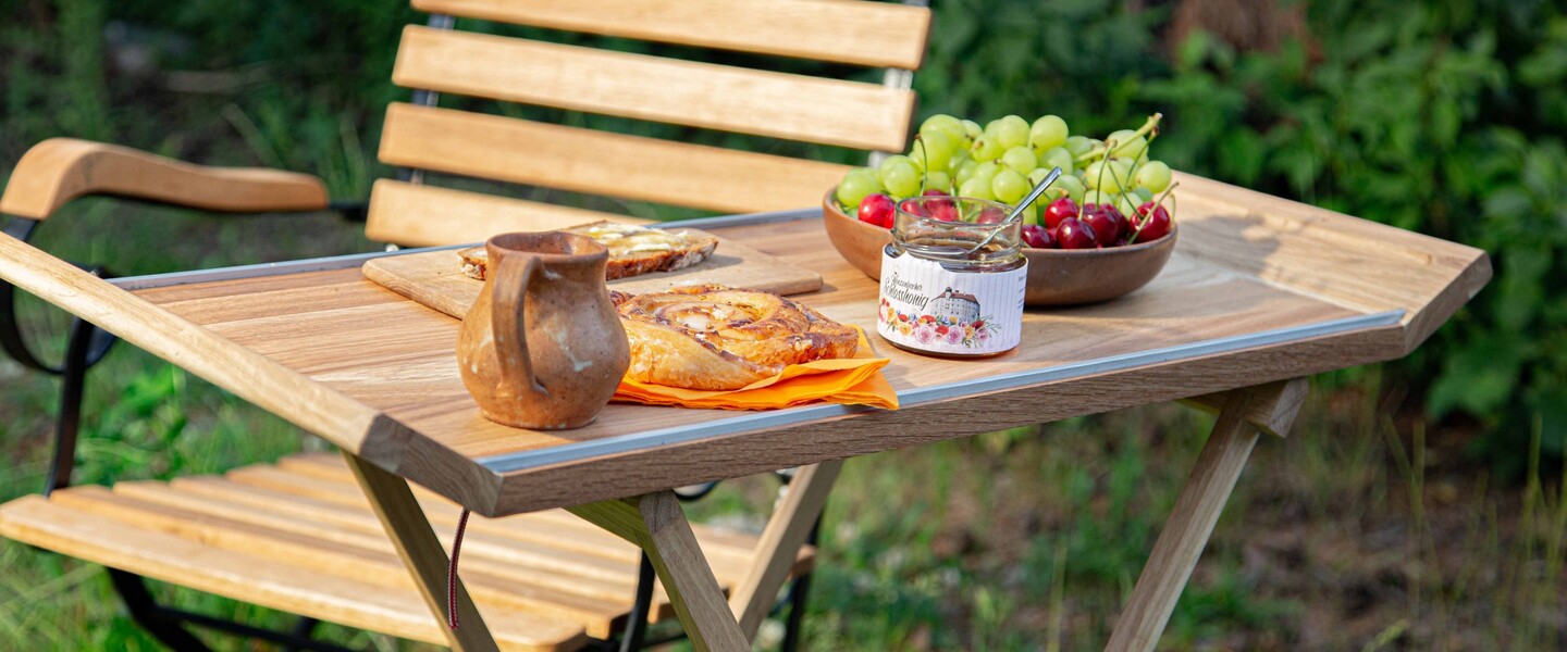 Auf einem kleinen Gartentisch stehen Obst, Marmelade und Kaffeest&uuml;ckchen