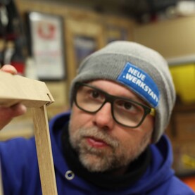 Robert Sike hält in Werkstatt Holzstücke aufeinander