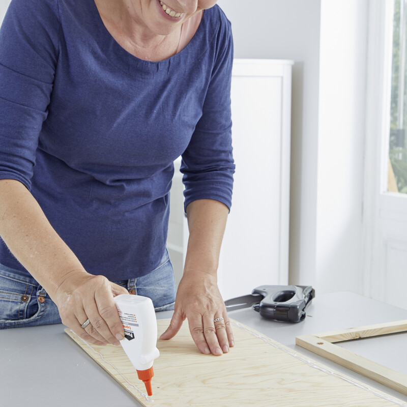 Eine Frau trägt Leim auf ein Holzbrett auf
