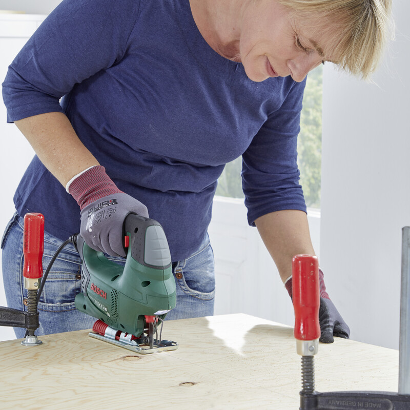 Eine Frau sägt mit einer Stichsäge ein Holzbrett zurecht.