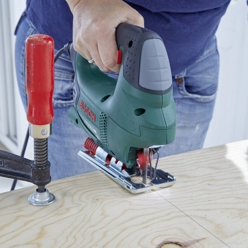 Ein Holzbrett wird mit einer Stichsäge zurecht gesägt.