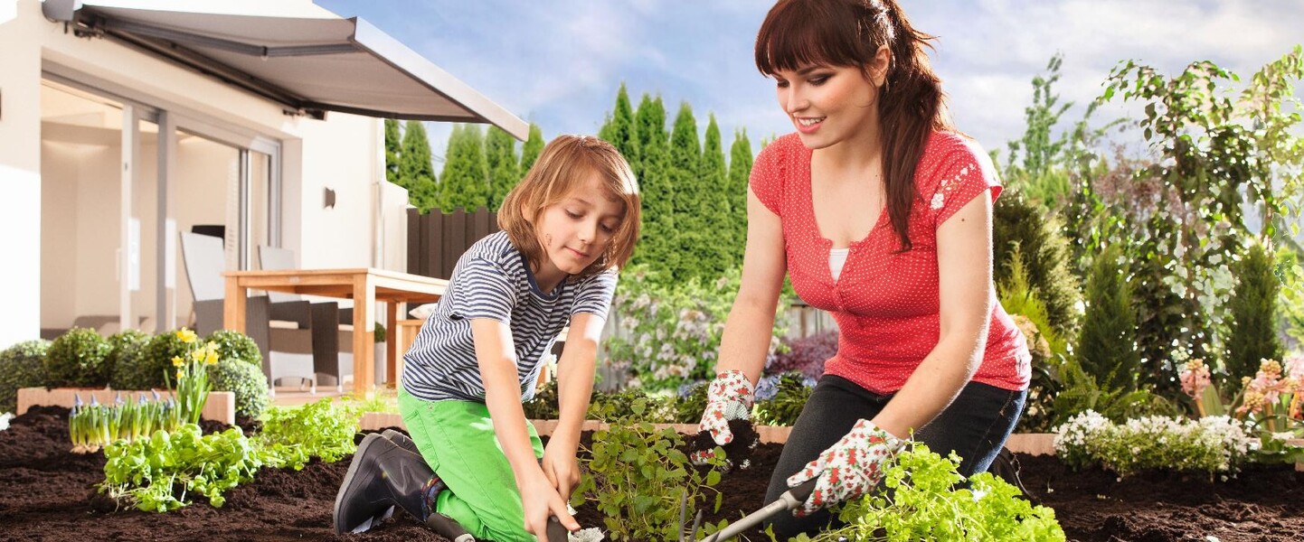 Eine Frau und ein Kind arbeiten gemeinsam im Garten an einem Beet