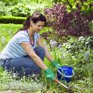 Frau hackt Unkraut im Blumenbeet