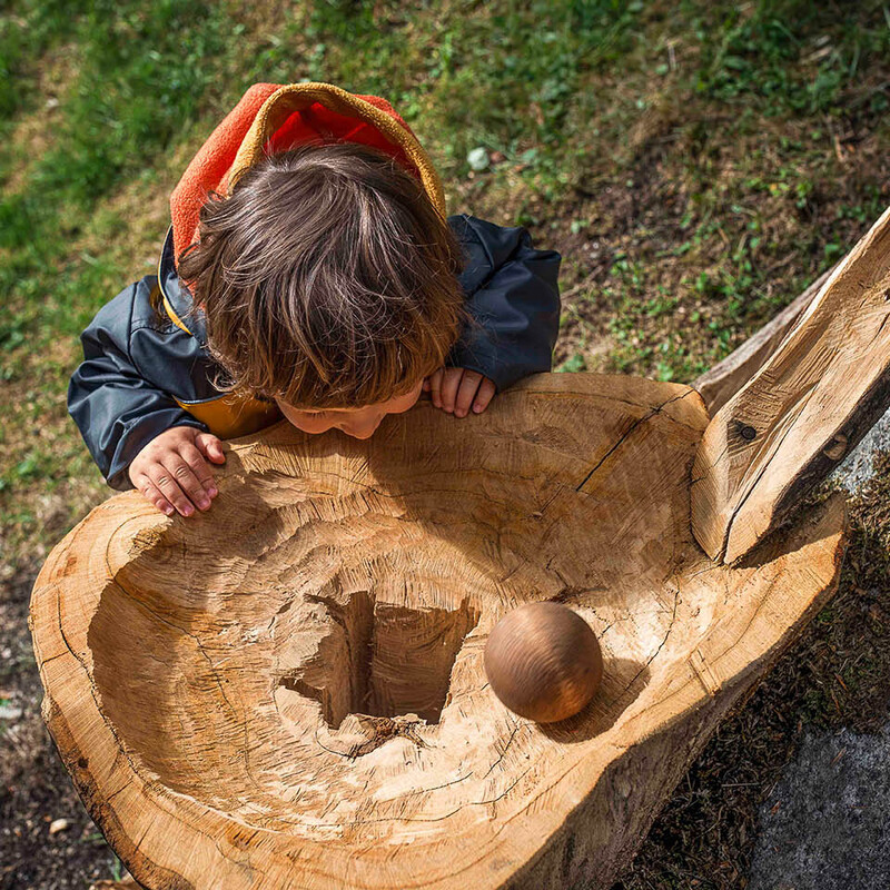 Kind schaut zu, wie eine große Holzkugel in das Loch eines Holztrichters rollt