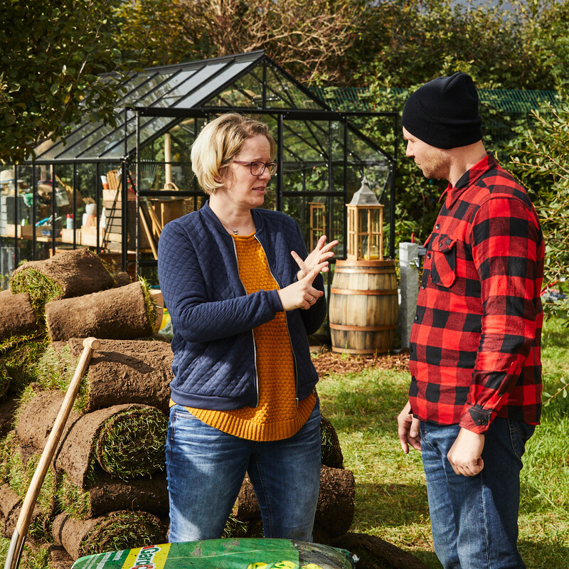 Paar steht im Garten neben dem zu verlegenden Rollrasen