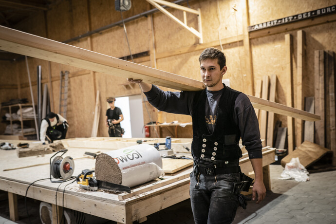Zimemrmann trägt Holzbalken durch die Werkstatt