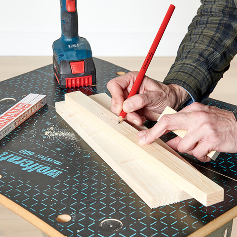 Mann zeichnet mit Bleistift Bohrmarkierungen auf Holzleiste