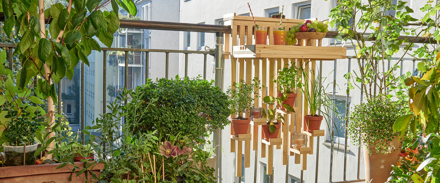 Selbstgebaute Balkonbar aus Holz mit Pflanzenregal hängt am Balkongeländer