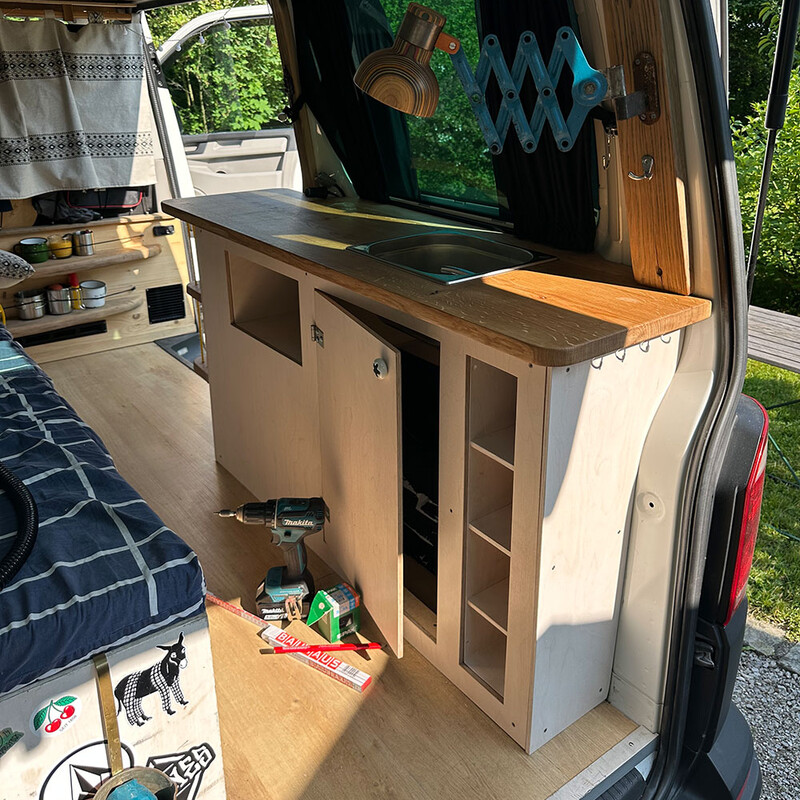 Werkzeug auf dem Boden neben DIY-Camper-Küche im Fahrzeug mit geöffneter Montageklappe