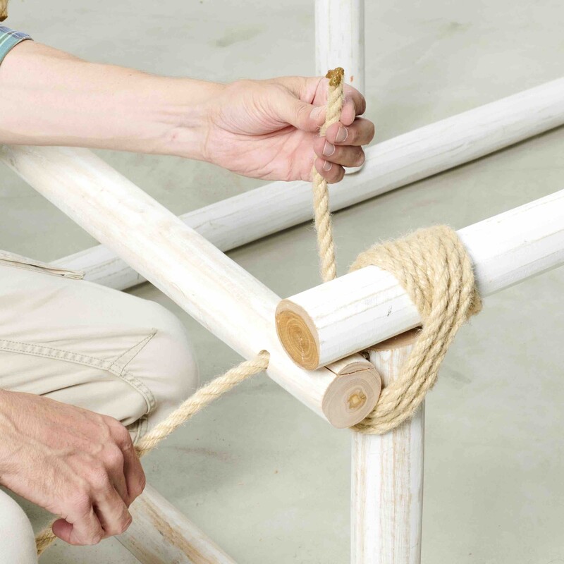 Mann führt Seil durch Loch in Holzstamm (DIY Daybed)