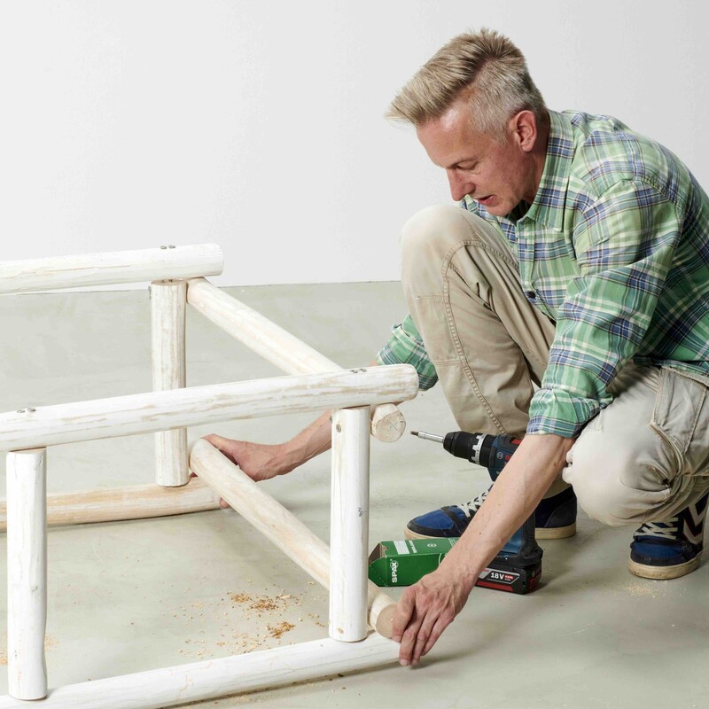 Mann kniet neben Daybed-Rahmen und positioniert die Teakholzstämme