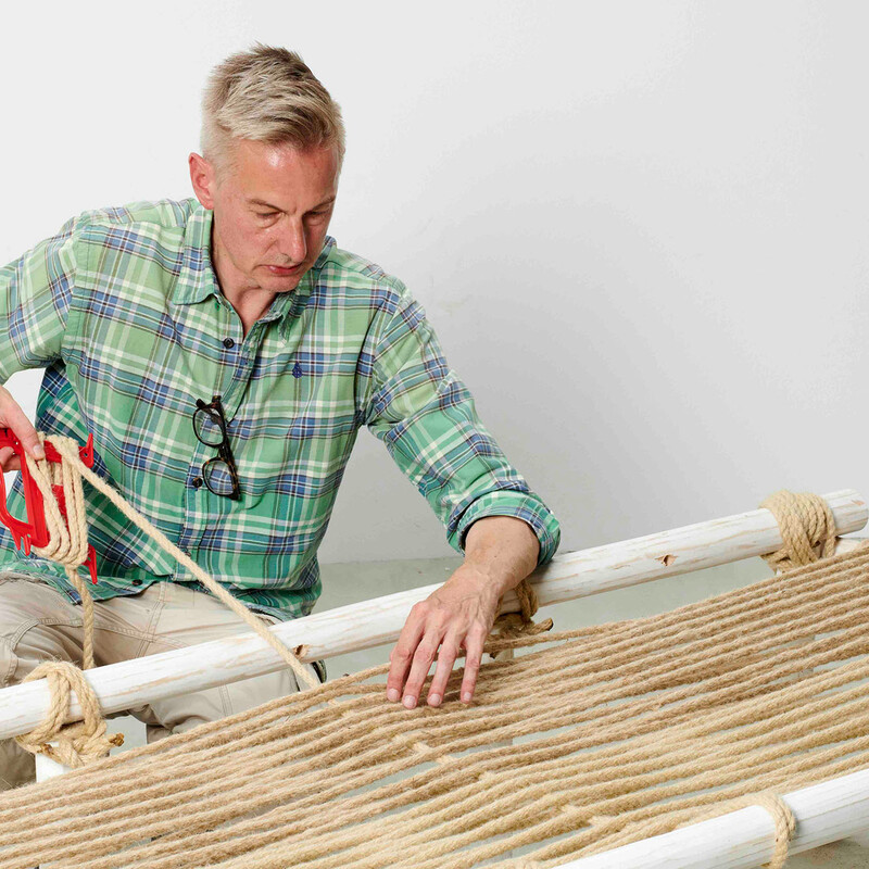Mann fädelt Seil für die Liegefläche eines selbstgebauten Daybeds aus Teakholz