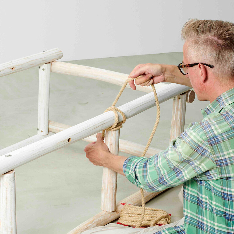 Mann wickelt Seil um Holzkonstruktion