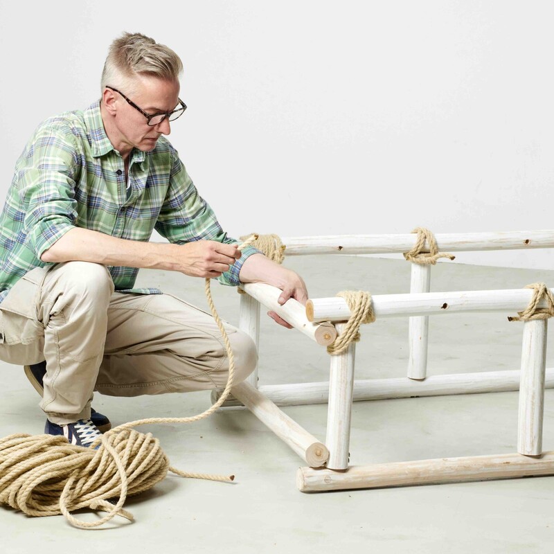 Mann hält Seil in der Hand und umwickelt damit den Rahmen eines selbstgebauten Daybeds aus Teakholz