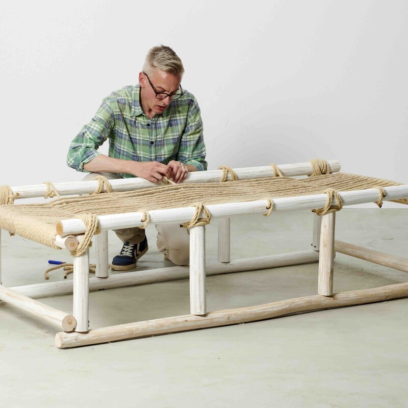 Mann sitzt neben selbstgebautem Daybed und konstruiert die Liegefläche aus Seil