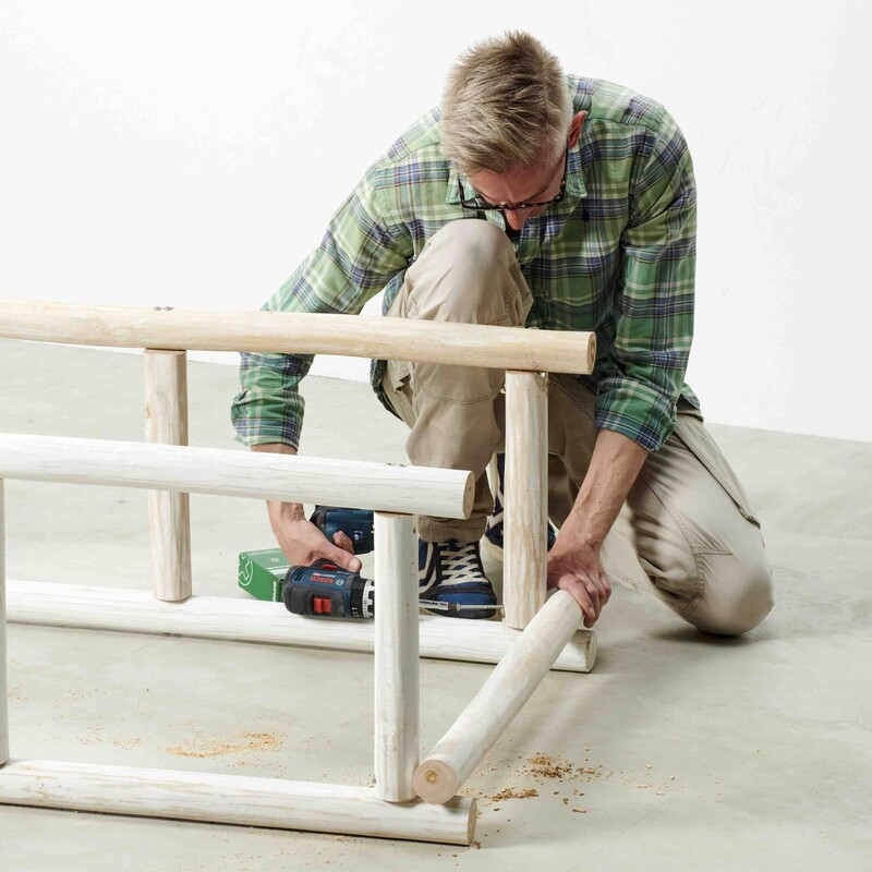 Mann kniet neben Daybed-Rahmen und schraubt mit Akkuschrauber Schrauben ins Holz