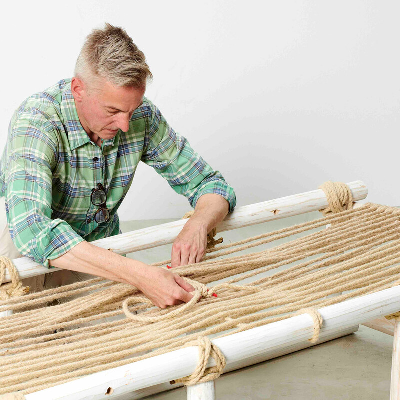 Mann fädelt Seil für die Liegefläche eines selbstgebauten Daybeds aus Teakholz