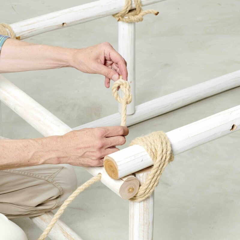 Mann verknotet Seil, um damit Holzstämme miteinander zu verbinden
