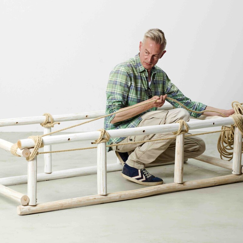 Man sitzt im Rahmen eines selbstgebauten Daybeds und spannt mit Seil die Liegefläge