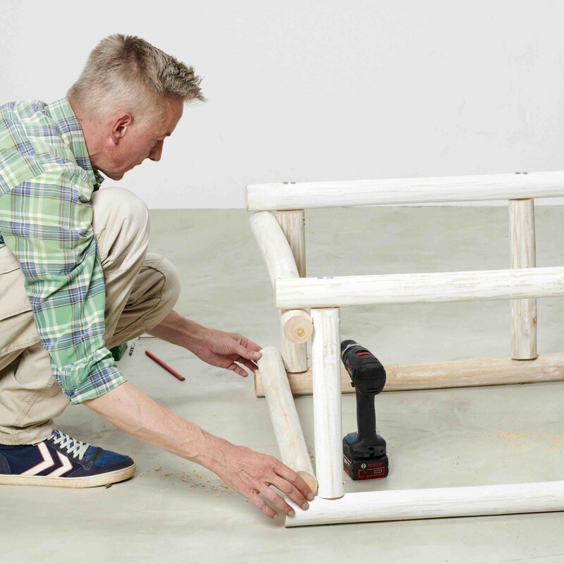 Mann kniet neben Daybed-Rahmen und positioniert die Teakholzstämme