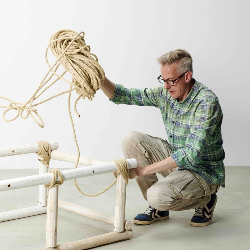 Mann sitzt neben selbstgebautem Daybed aus Holz und hält Seil in der Hand