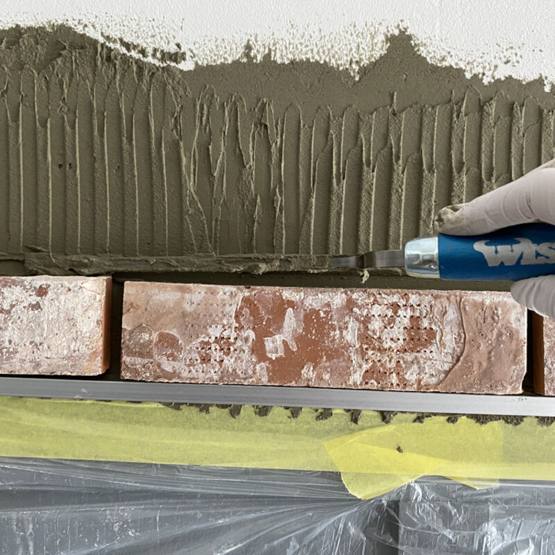 Arbeiten mit der Fugenkelle beim Verkleiden einer Wand mit Klinkersteinen