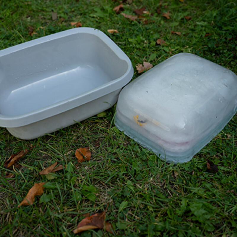 Neben einer quadratischen Plastikschüssel liegt ein quadratischer Eisblock auf dem Kopf