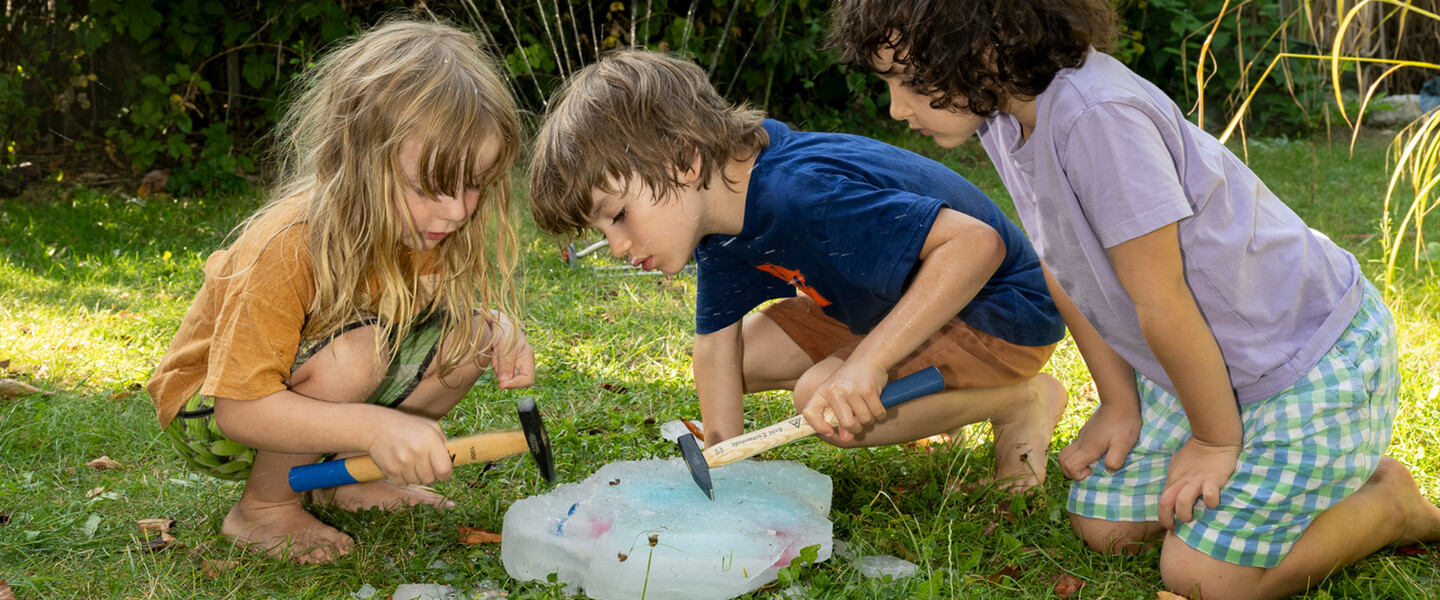 Kinder klopfen in einem Garten mit H&auml;mmern auf einen Eisblock mit Sch&auml;tzen wie z.B. Plastik-Tieren