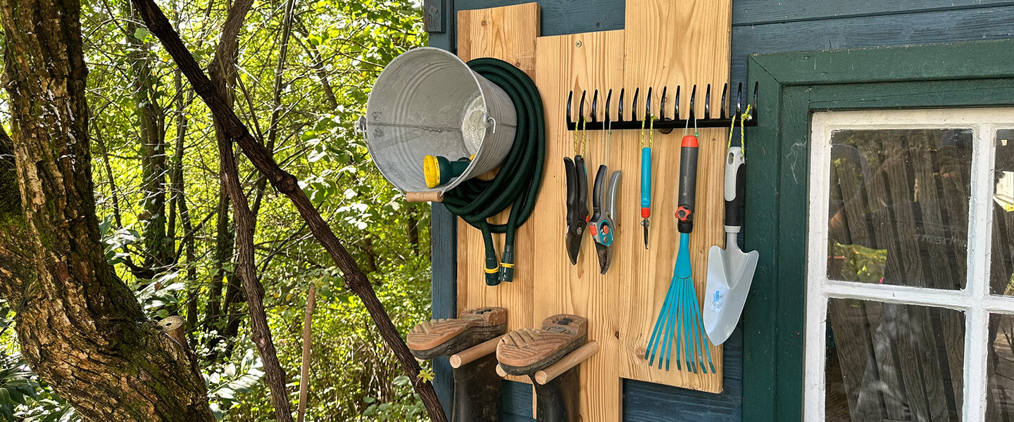 Selbstgebautes Garten-Organizer-Regal mit Gummistiefeln und Werkzeugen hängt an Hauswand