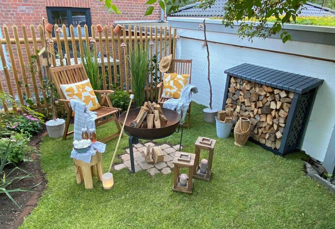 Umgestaltete Gartenecke mit Rollrasen, Feuerschale, Feuerholzregal und Lichterkette