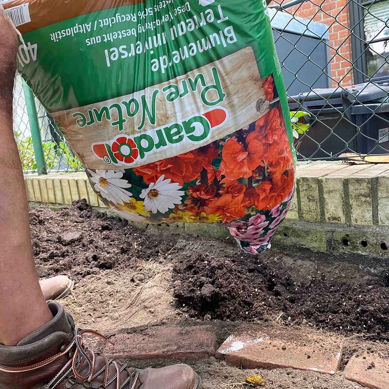 Sack Blumenerde wird ausgeleert im neuen Beet