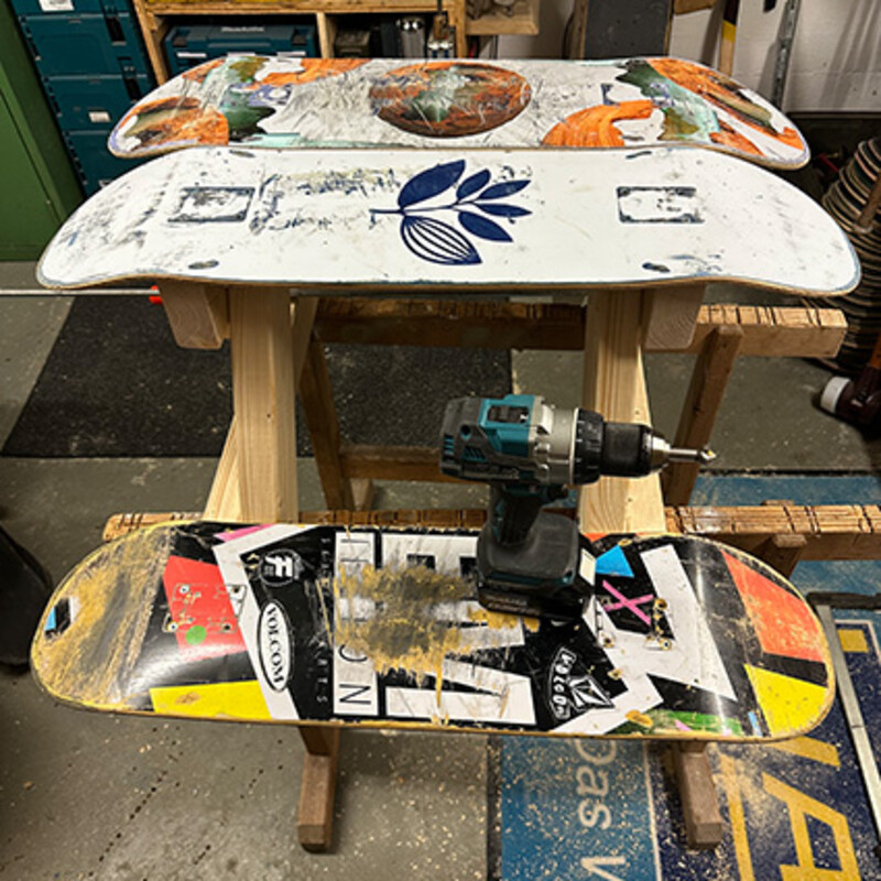 Drei Skateboards und ein Akku-Schrauber liegen auf einer Tisch-Unterkonstruktion auf zwei Schreinerwinkeln