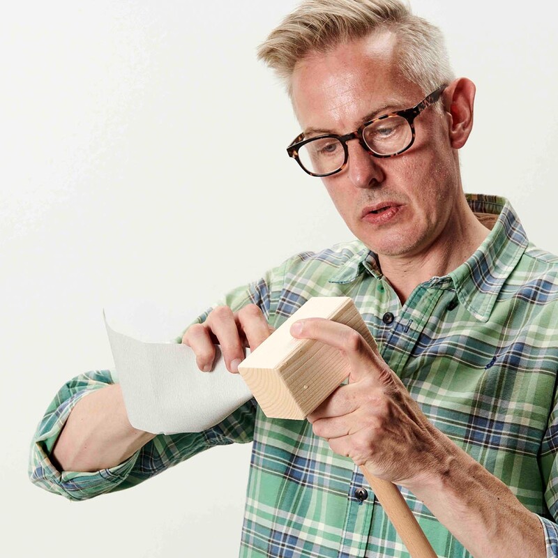 Mann mit Brille und Karohemd schleift einen selbstgemachten Holzschläger (Krocket)