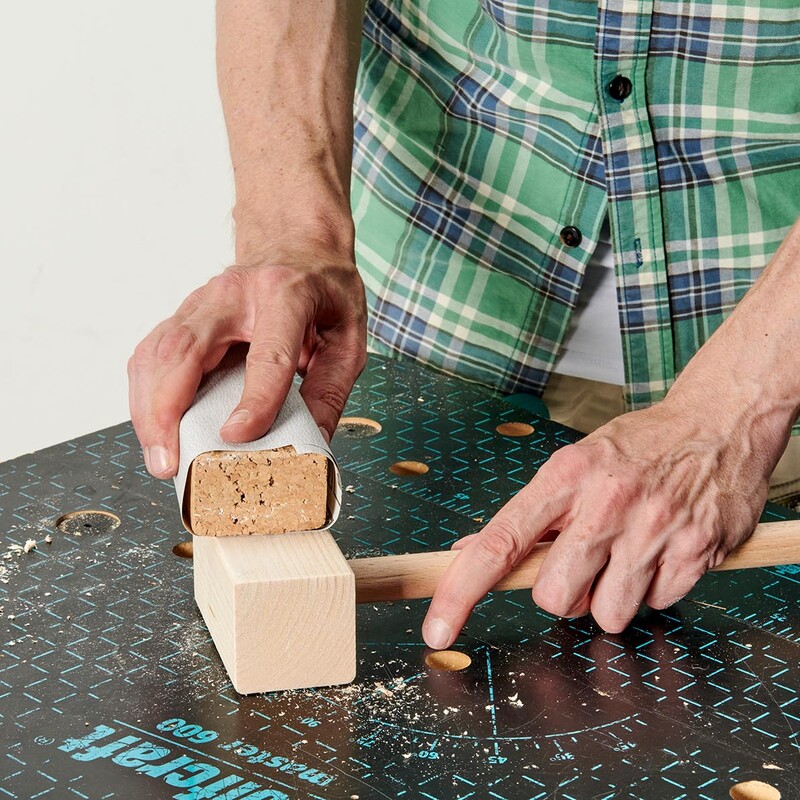 Mann hält Schleifpapier und schleift per Hand einen Krocketschläger aus Holz
