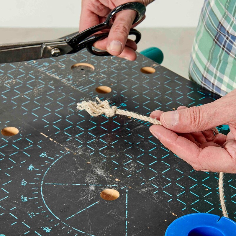 Mann hält eine Schere in der einen und eine Kordel mit Knoten in der anderen Hand
