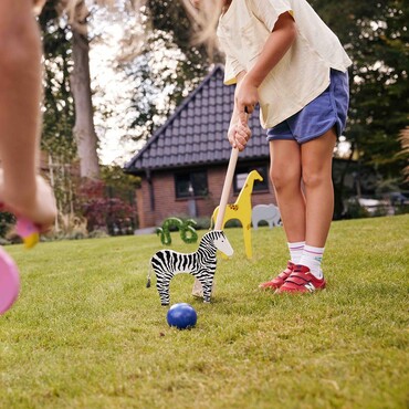 zwei Kinder spielen Krocket mit bunten Tierfiguren im Garten