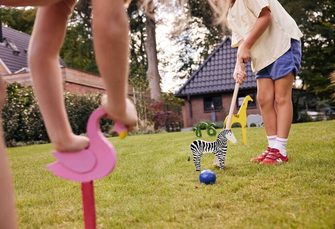 zwei Kinder spielen Krocket mit bunten Tierfiguren im Garten