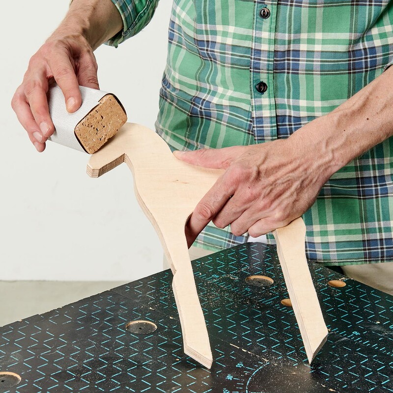 Mann schleift eine Tierfigur aus Holz mit der Hand ab