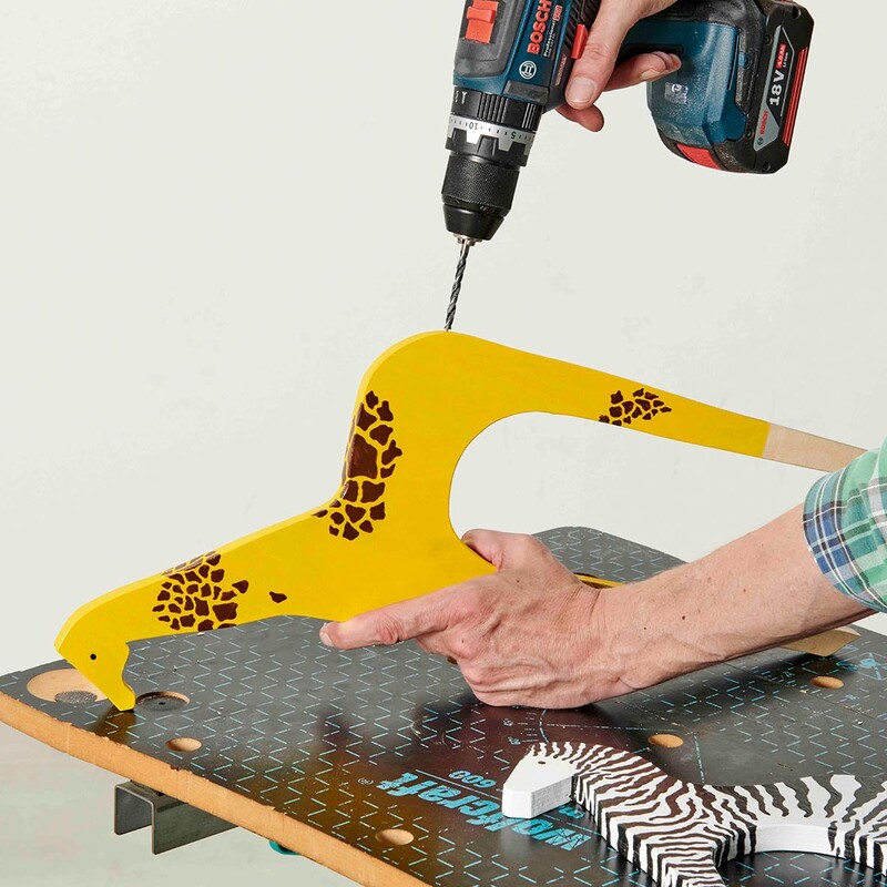 Mann bohrt mit Schlagbohrschrauber ein Loch in eine gelbe Tierfigur (Giraffe)