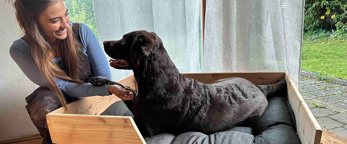 Junge Frau sitzt neben selbstgebauten Hundebett aus Holz