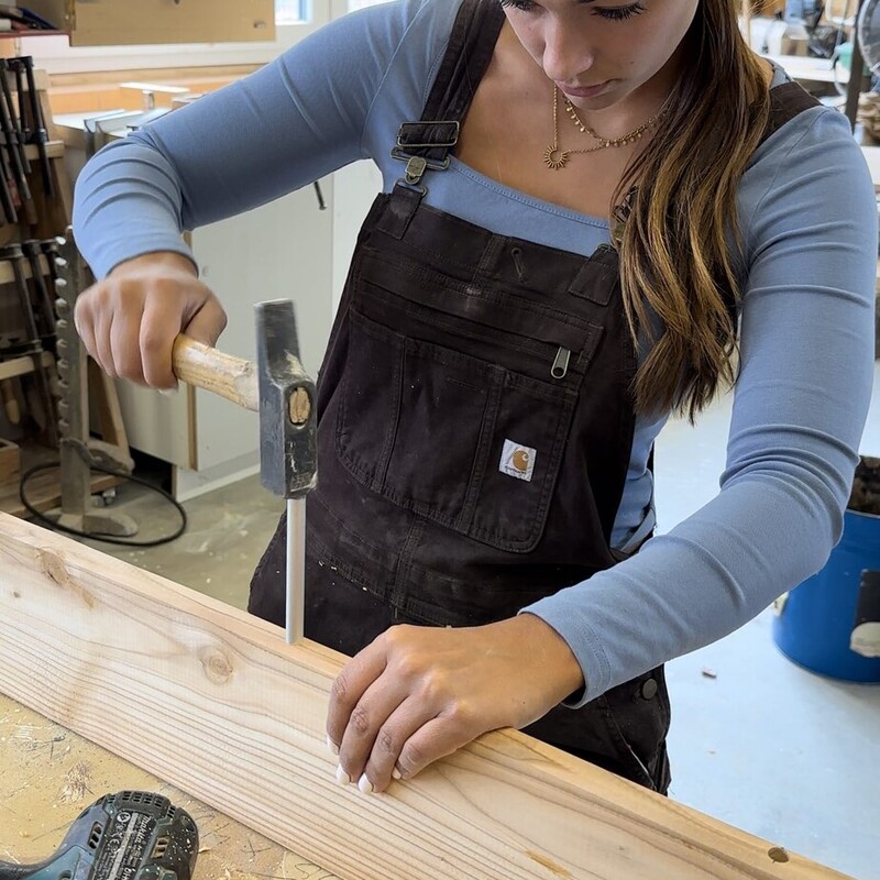 Frau in Werkstatt schlägt Metallrohr in Holz